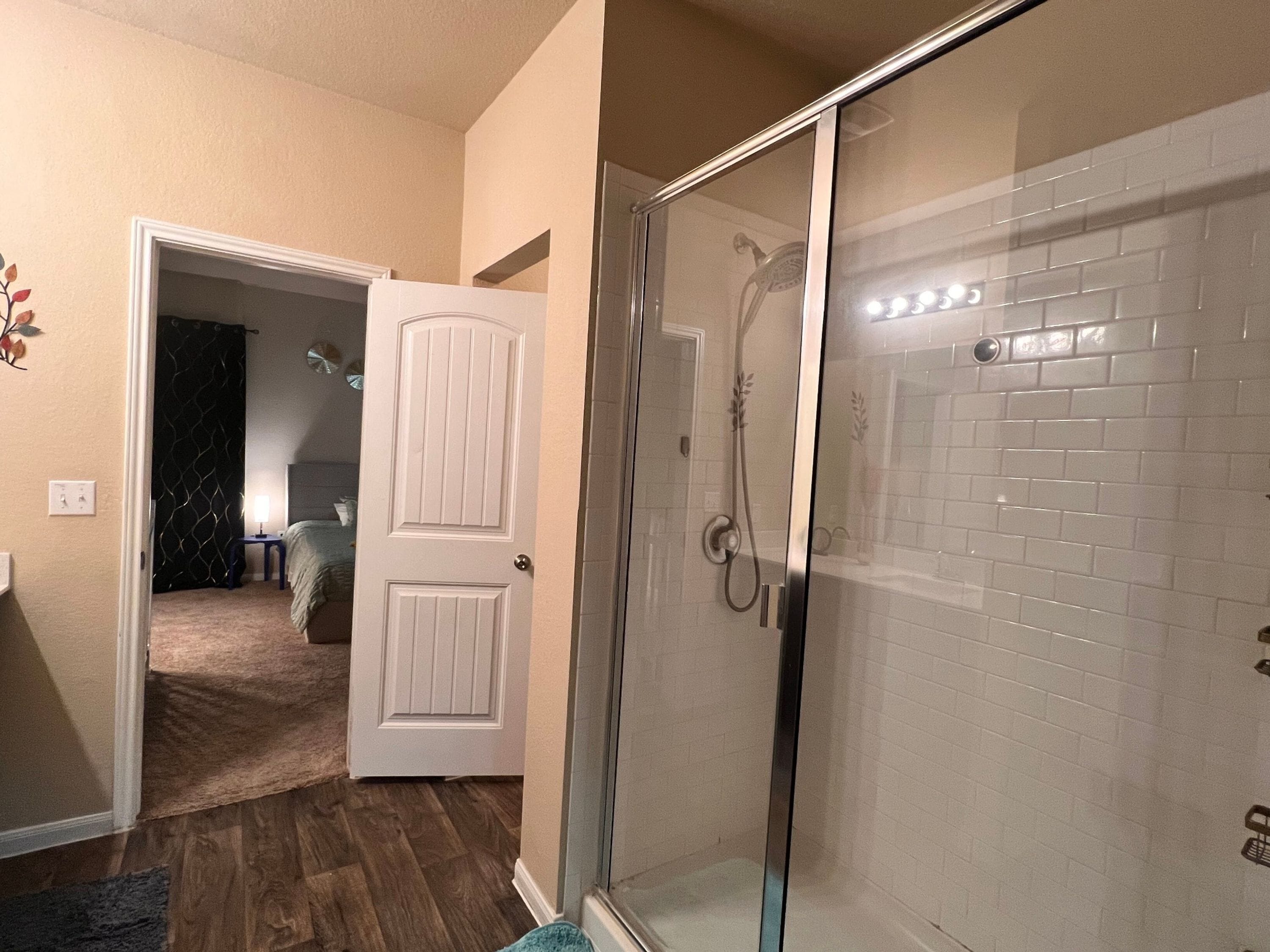 A hotel bathroom with a glass-enclosed shower, a white door, and a tiled wall.