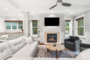 A modern living room with a fireplace, a flat-screen TV, and a ceiling fan. - The Emerald at 30A: Heated Pool, Golf Cart and Bikes INCLUDED (Santa Rosa Beach)