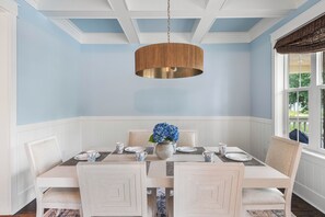 A dining room with a table set for four, a hanging light fixture, and a window with a view of greenery. - The Emerald at 30A: Heated Pool, Golf Cart, Bikes (Santa Rosa Beach)