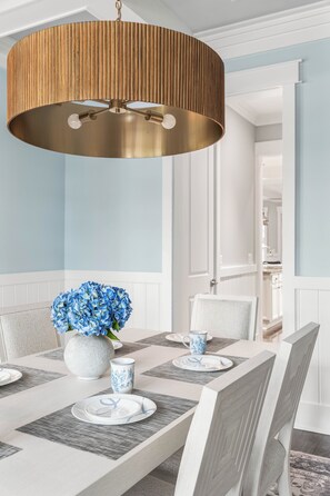A dining area with a round table, chairs, a vase with flowers, and a hanging light fixture. - The Emerald at 30A: Heated Pool, Golf Cart and Bikes INCLUDED (Santa Rosa Beach)