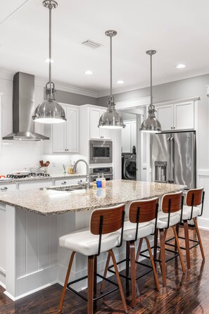 A modern kitchen with a central island, bar stools, stainless steel appliances, and pendant lighting. - The Emerald at 30A: Heated Pool, Golf Cart and Bikes INCLUDED (Santa Rosa Beach)