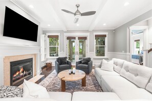 A modern living room with a fireplace, a flat-screen TV, and a ceiling fan. - The Emerald at 30A: Heated Pool, Golf Cart, Bikes (Santa Rosa Beach)