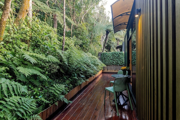 An outdoor wooden deck with a table and chairs, surrounded by dense green foliage.