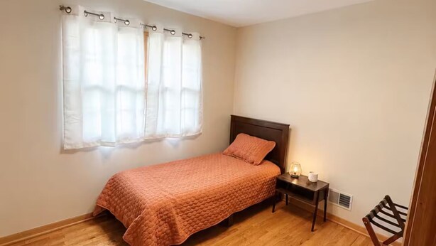 A bedroom with a single bed, a nightstand, a lamp, and a window with curtains. - Midtown Omaha Near Everything! No Cleaning Fee! (Omaha)