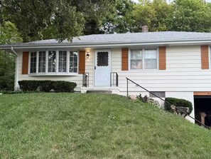 A two-story house with a front porch, a garage, and a well-maintained lawn. - Midtown Omaha Near Everything! No Cleaning Fee! (Omaha)