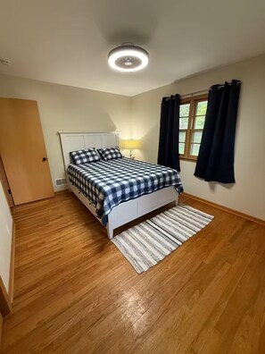 A bedroom with a bed, a nightstand, a window with curtains, and a ceiling light. - Midtown Omaha Near Everything! No Cleaning Fee! (Omaha)