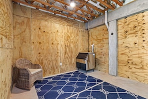 Ein Zimmer mit Holzwänden, einem Korbsessel, einem Heizgerät und einem gemusterten Teppich.