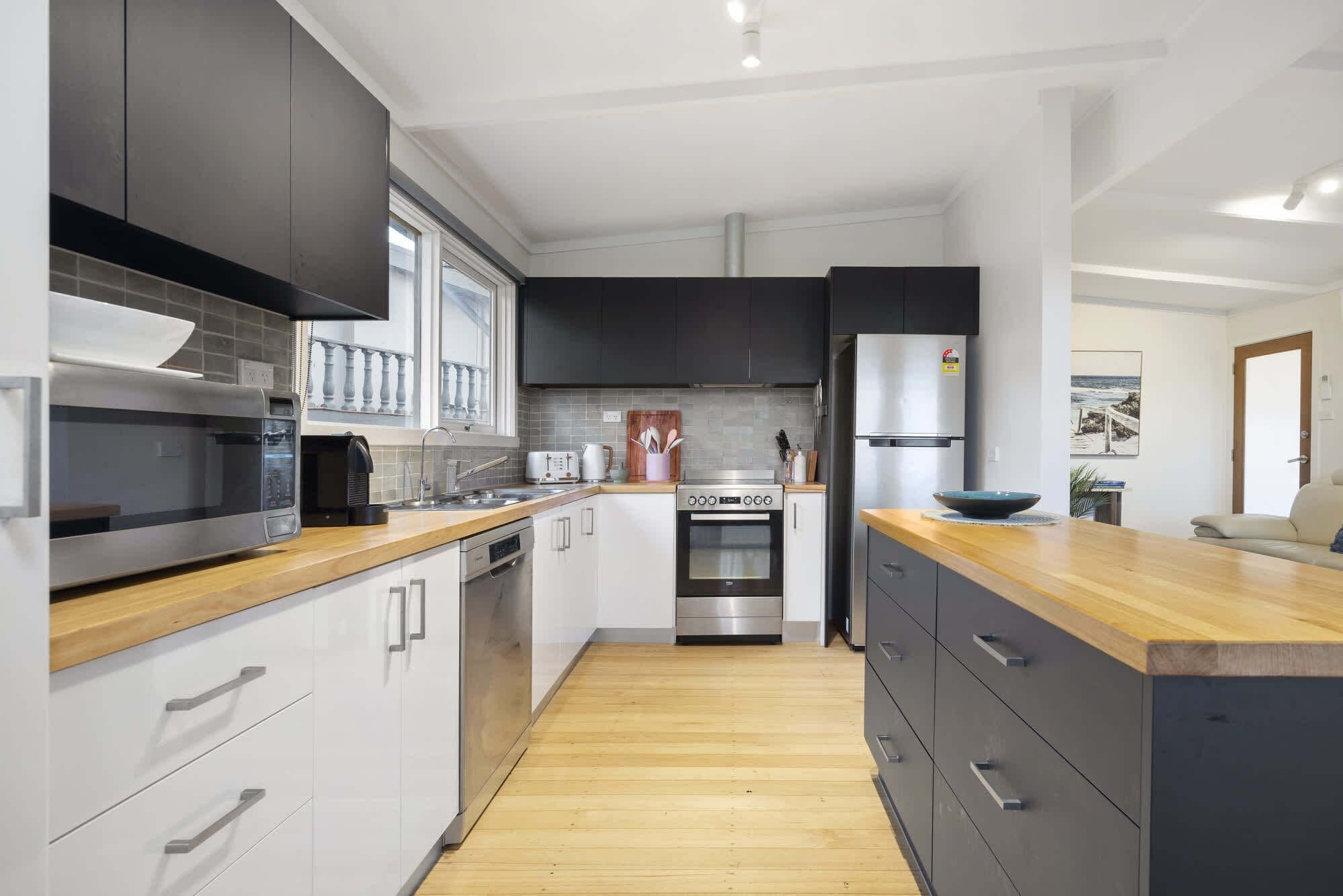 A modern kitchen with stainless steel appliances, a wooden countertop, and a view of the living area.