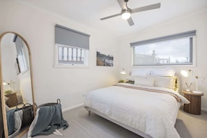 Ein Schlafzimmer mit einem Bett, einem Deckenventilator, einem Fenster mit Blick, einem Nachttisch mit Lampe und einem Spiegel.