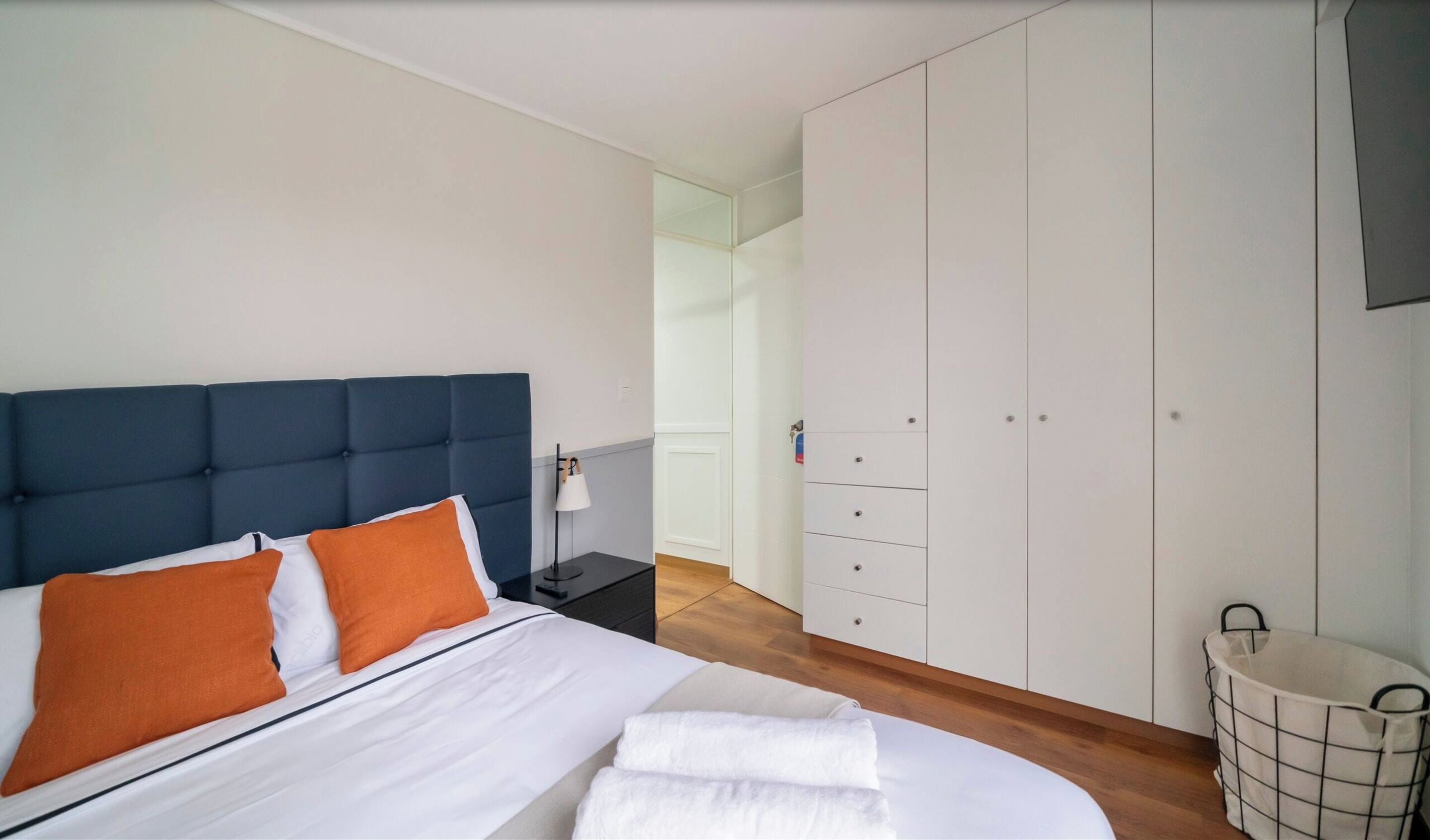 Et soveværelse med seng, garderobe, natbord og lampe.