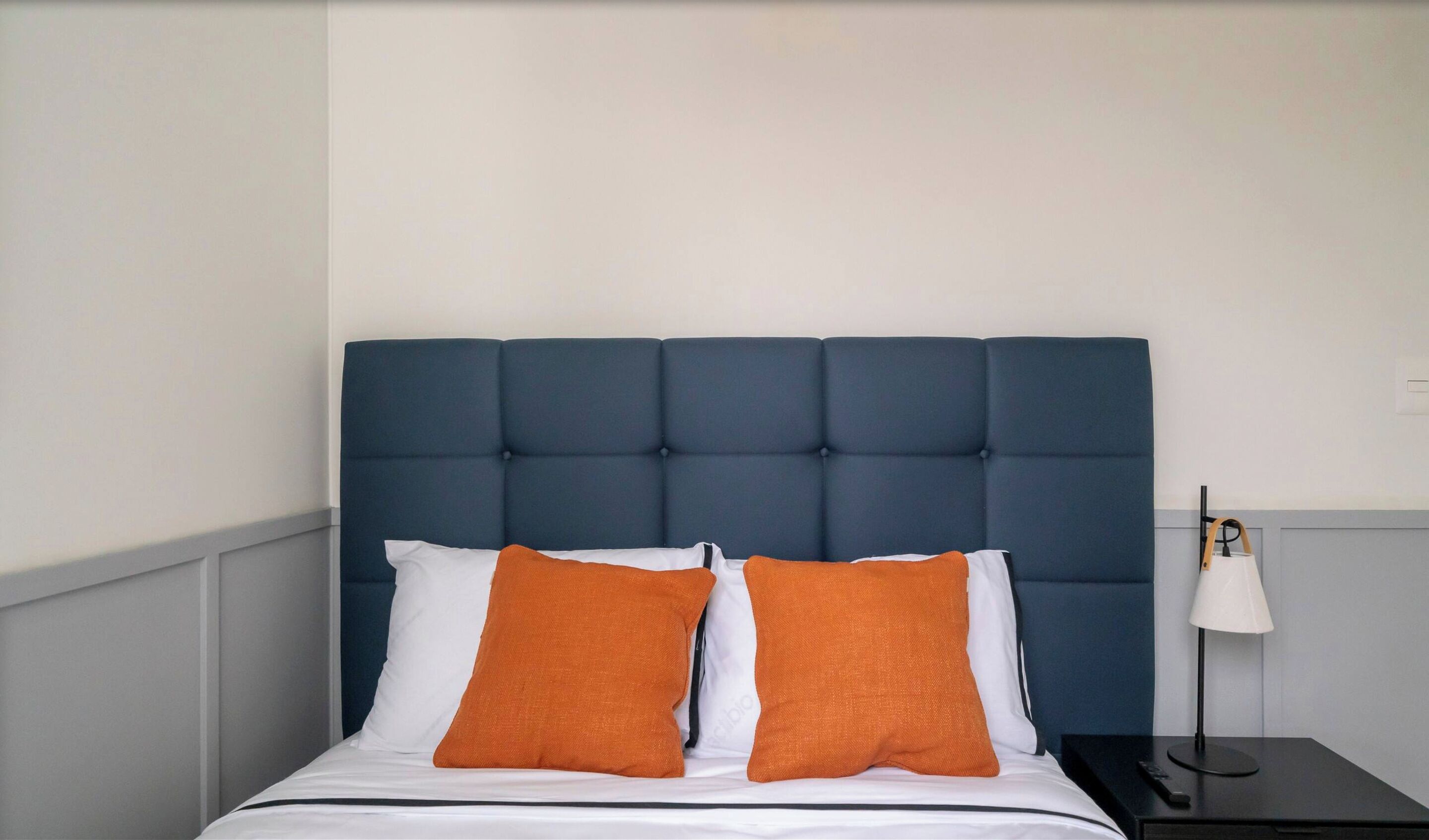 Ein Bett mit dunkelbrauner Kopfteile, weißer Bettwäsche und zwei orangefarbenen Kissen.