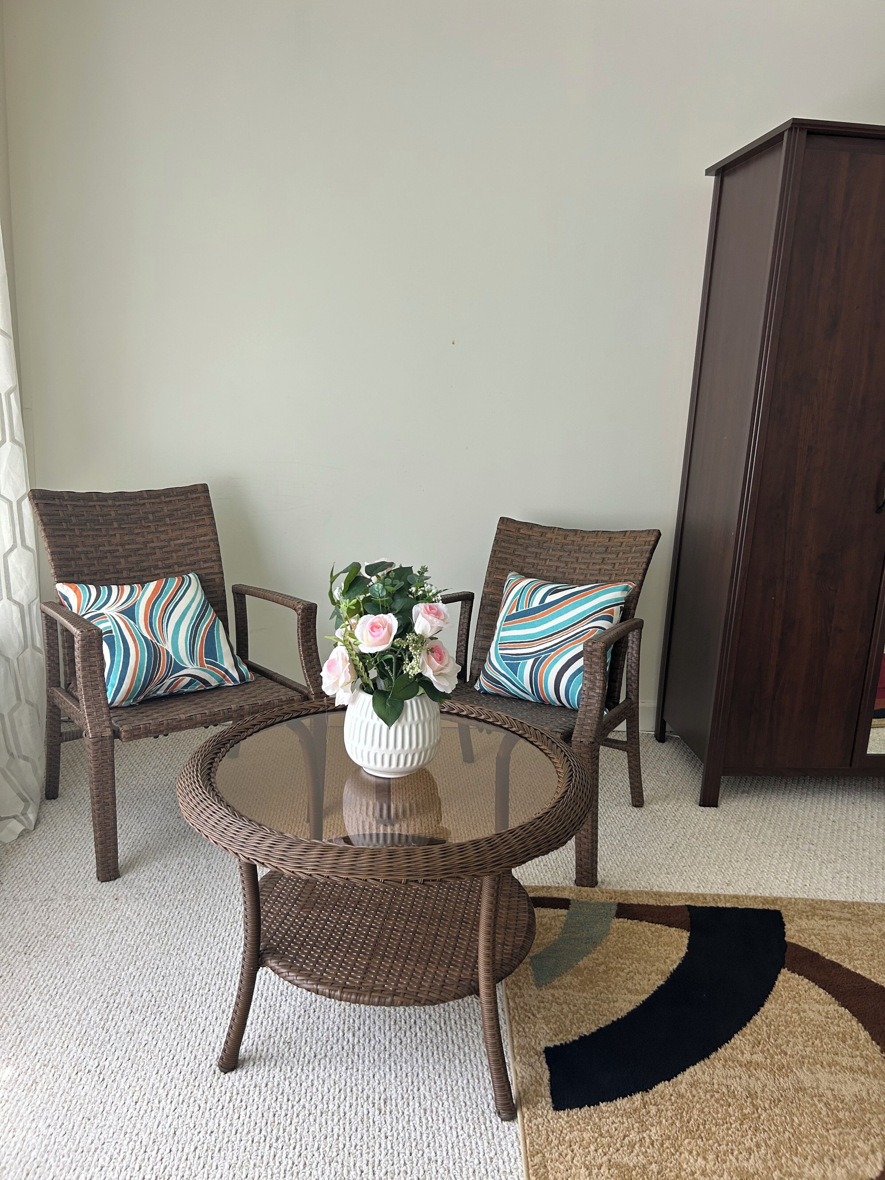 A room with two wicker chairs, a glass table, and a cabinet.