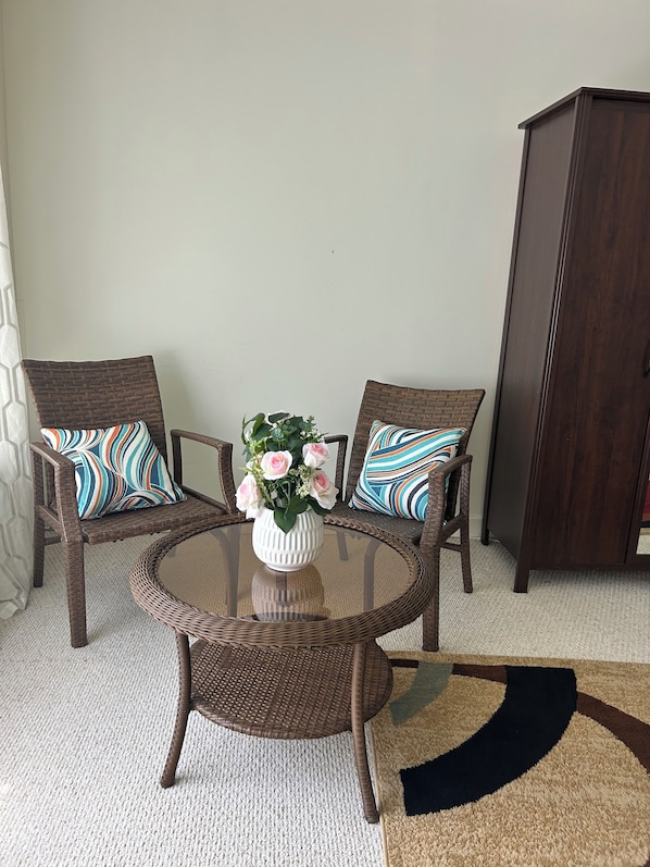 A room with two wicker chairs, a glass table, and a cabinet.