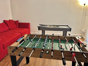 Ein Kicker-Tisch in einem Raum mit einem roten Sofa und einem Billardtisch.
