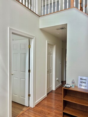 A hallway with white doors, a wooden floor, and a sign indicating a shoe storage area.