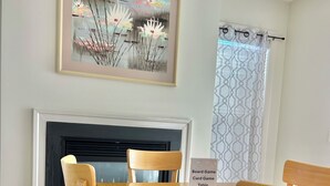 A dining area with a wooden table and chairs, a fireplace, and a framed artwork above the mantel.