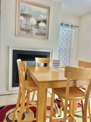 A dining area with a wooden table and chairs, a fireplace, and a framed artwork above the mantel.