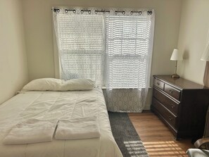 A bedroom with a bed, a dresser, a nightstand, and a window with curtains.