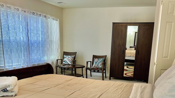 A hotel room with a large bed, two chairs, a wardrobe, and a window with blinds.
