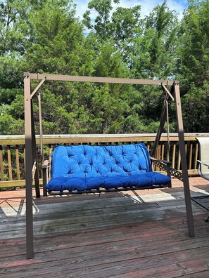 Eine Holzliege mit blauer gepolsterten Sitzfläche und Rückenlehne, auf einer Holzterrasse mit Geländer.