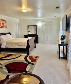 A bedroom with a bed, a bedside table, a mirror, a carpet, and a wall-mounted TV.