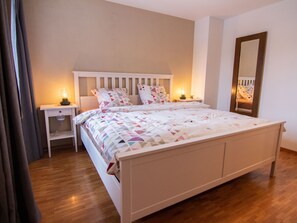 Un dormitori amb un llit doble, dues taules de nit amb làmpades, un calaix i un paviment de fusta.
