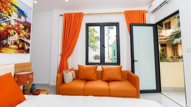 A modern hotel room with a bed, orange sofa, and a large window with curtains. - Aura Retreat Boutique Hotel Hanoi (Hanoi)