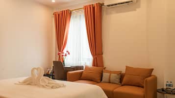 A hotel room with a bed, a sofa, a table with a vase of flowers, and an air conditioning unit.
