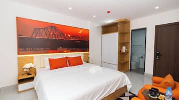 A hotel room with a bed, a large painting of a bridge, a wardrobe, a bathroom, and a seating area with a table.