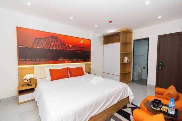 A hotel room with a bed, a large painting of a bridge, a wardrobe, a bathroom, and a seating area with a table. - Aura Retreat Boutique Hotel Hanoi (Hanoi)
