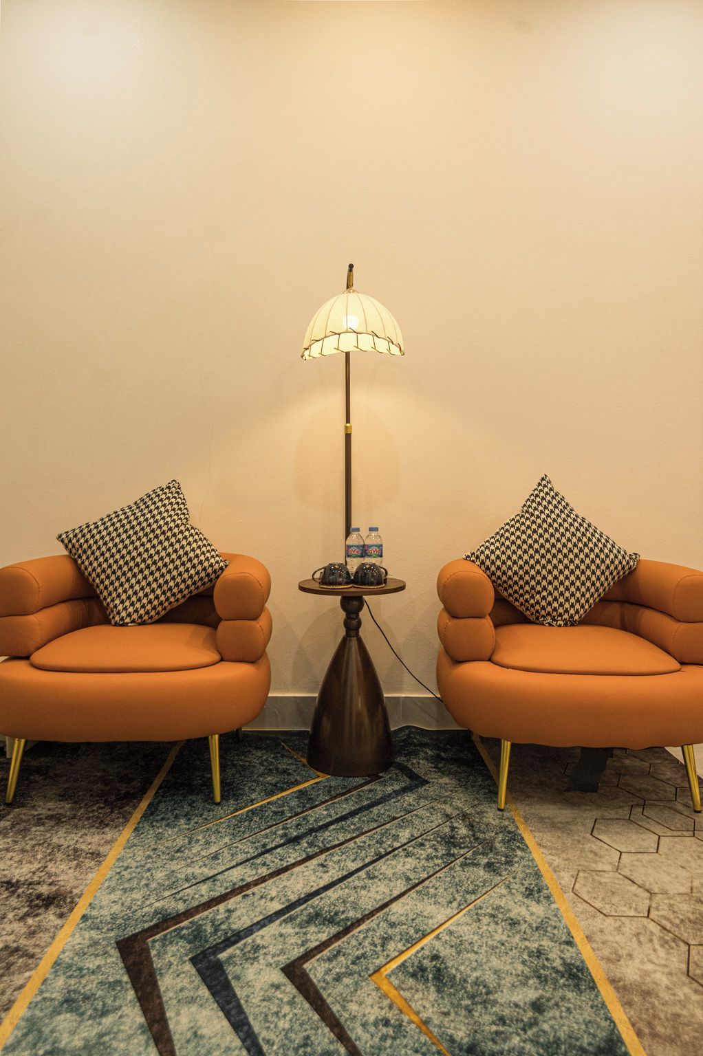 A room with two orange armchairs, a floor lamp, and a small table with water bottles.