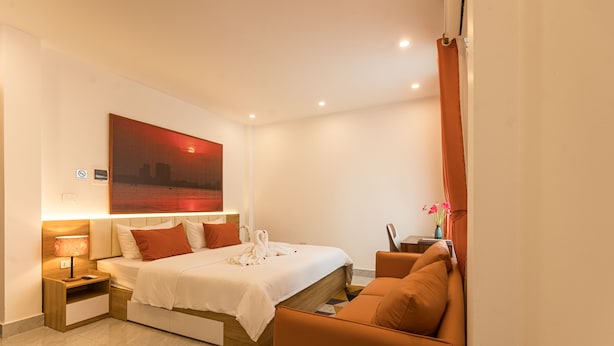 Habitación de hotel con una cama, un sofá, una mesita de noche, una lámpara y un cuadro en la pared.