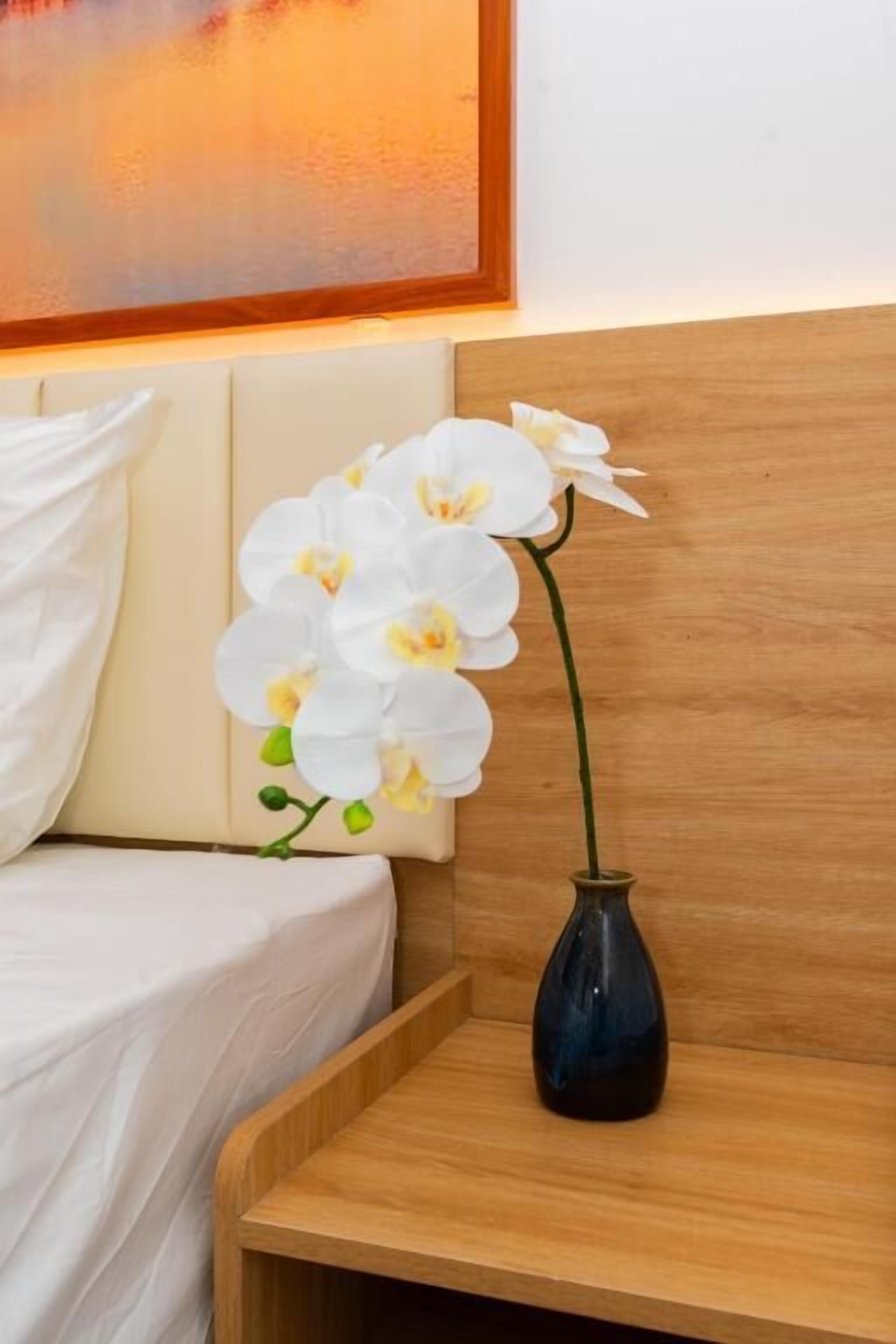 A wooden bedside table with a dark vase containing white orchids.
