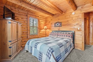 A cabin-style bedroom with a wooden ceiling, a bed with a patterned blanket, a window with a view of trees, and a wall-mounted lamp. - Fabulous Luxury Log Home, 6BR/4BA Hot Tub, 3 Min Drive to Base (Ludlow)
