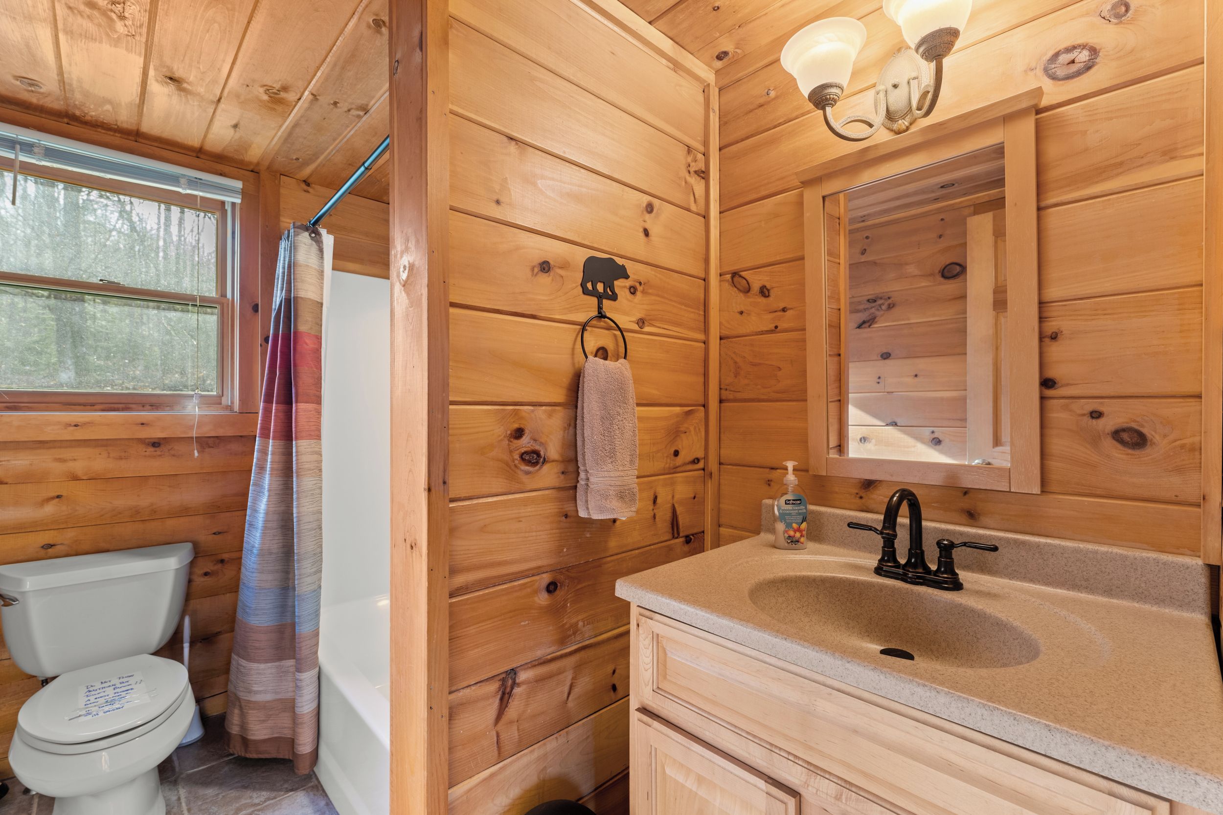 Ein Badezimmer in einer Holzhütte mit Toilette, Dusche, Waschbecken und einem Handtuch an einem Haken.
