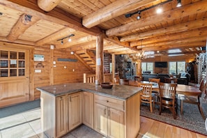A log cabin interior with a kitchen area, dining space, and a stone fireplace. - Fabulous Luxury Log Home, 6BR/4BA Hot Tub, 3 Min Drive to Base (Ludlow)