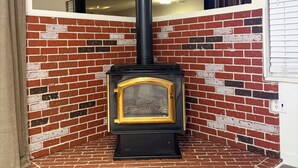 A wood-burning stove with a black chimney, set against a brick wall with a white trim.