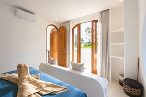 A hotel room with a bed, a window with curtains, a view of greenery outside, and a wall-mounted air conditioning unit. - 2BR Private Pool Villa Near Batu Bolong & La Brisa (Badung)