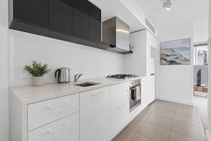 A modern kitchen with white cabinetry, a stainless steel range hood, a gas stove, a sink, and a potted plant. - Sheraton Little Collins by Ready Set Stay (Melbourne)