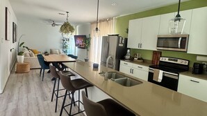 A modern kitchen with a central island, bar stools, a dining area with a sofa, and a view of the living room. - 3BR home w/ AC, parking & W/D near Galleria/ Downtown (Houston)