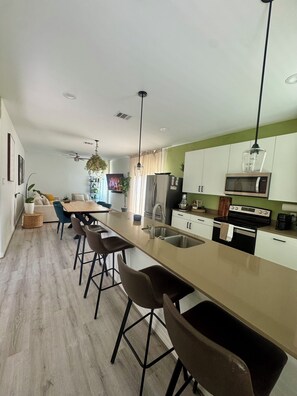 Eine moderne Küche mit einer zentralen Kochinsel, Barhocker, einem Essbereich mit einer Couch und Blick auf das Wohnzimmer.