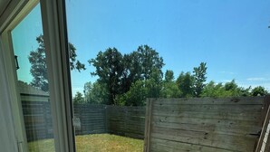 A view through a glass door to a backyard with a wooden fence, a concrete patio, and trees in the background. - 3BR home w/ AC, parking & W/D near Galleria/ Downtown (Houston)