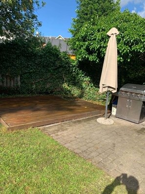 Un patio trasero con una terraza de madera, una parrilla y un parasol.