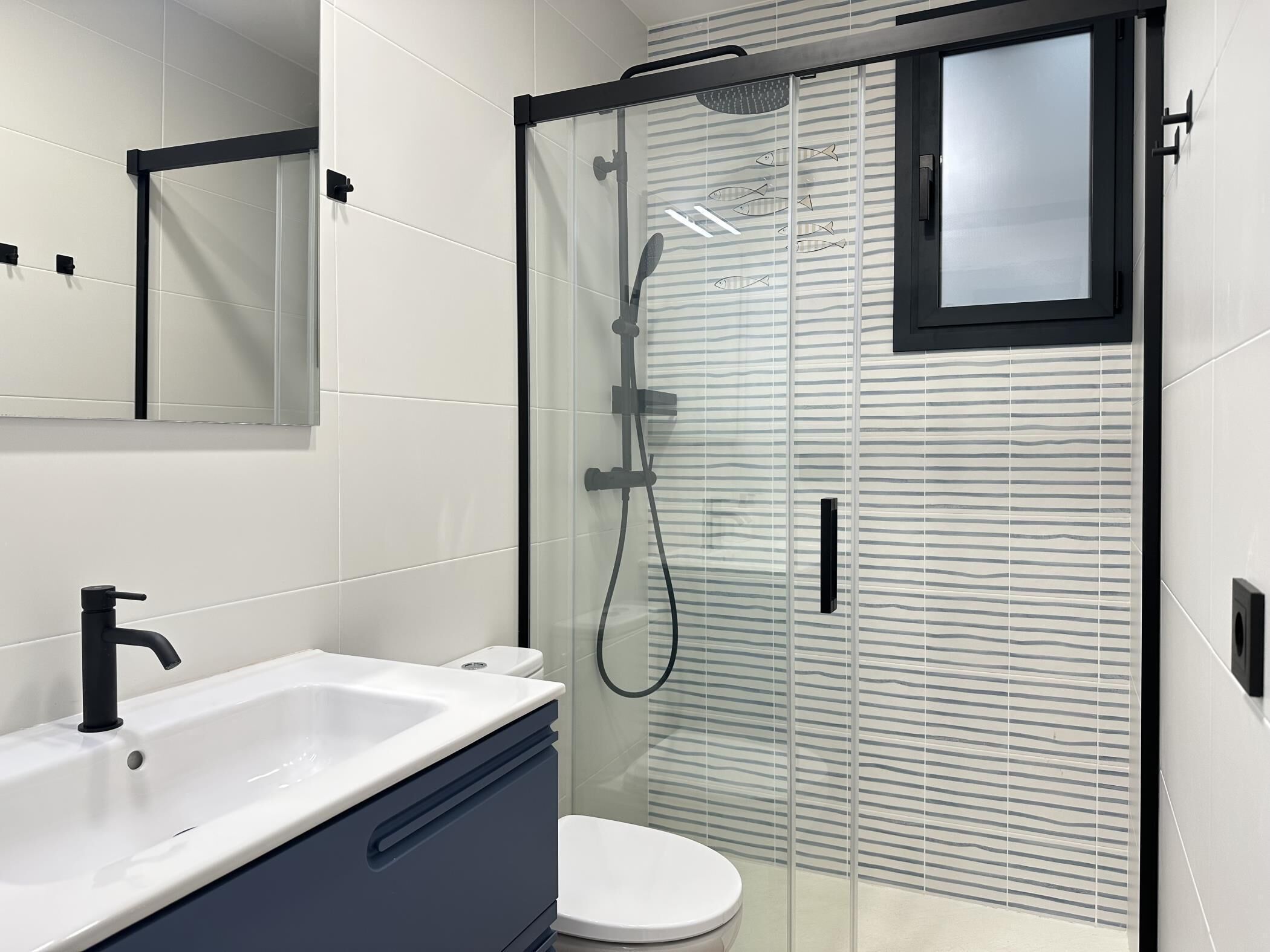 Une salle de bain moderne avec un lavabo blanc, un robinet noir et une douche séparée par une paroi de verre.