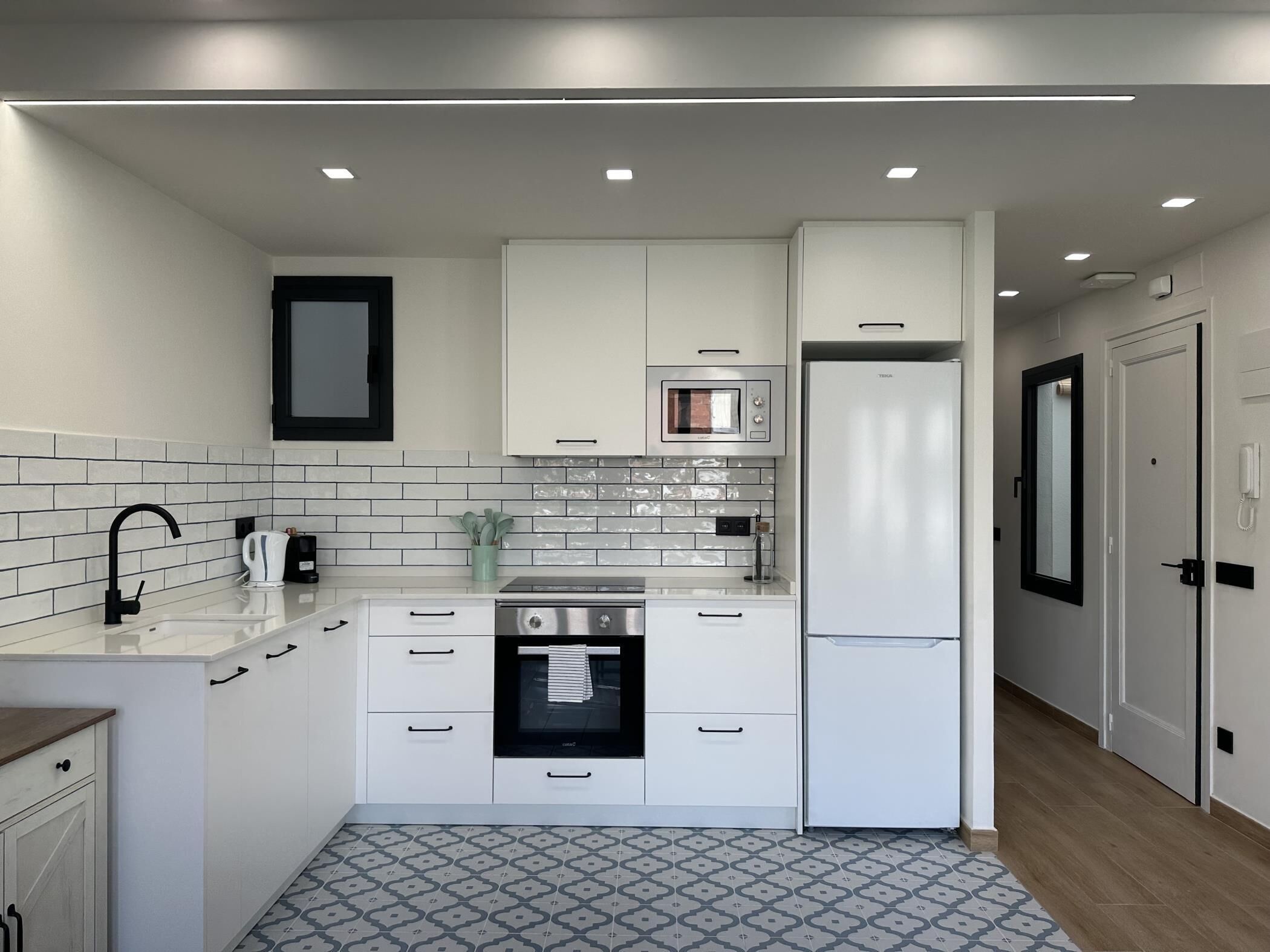 A modern kitchen with white cabinetry, a built-in oven, a refrigerator, and a tiled backsplash.