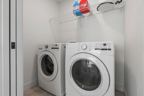Two front-loading washing machines in a laundry room with a metal rack above them. - Creekstone Retreat - South West Calgary - A Cozy Home for a Peaceful stay (Calgary)