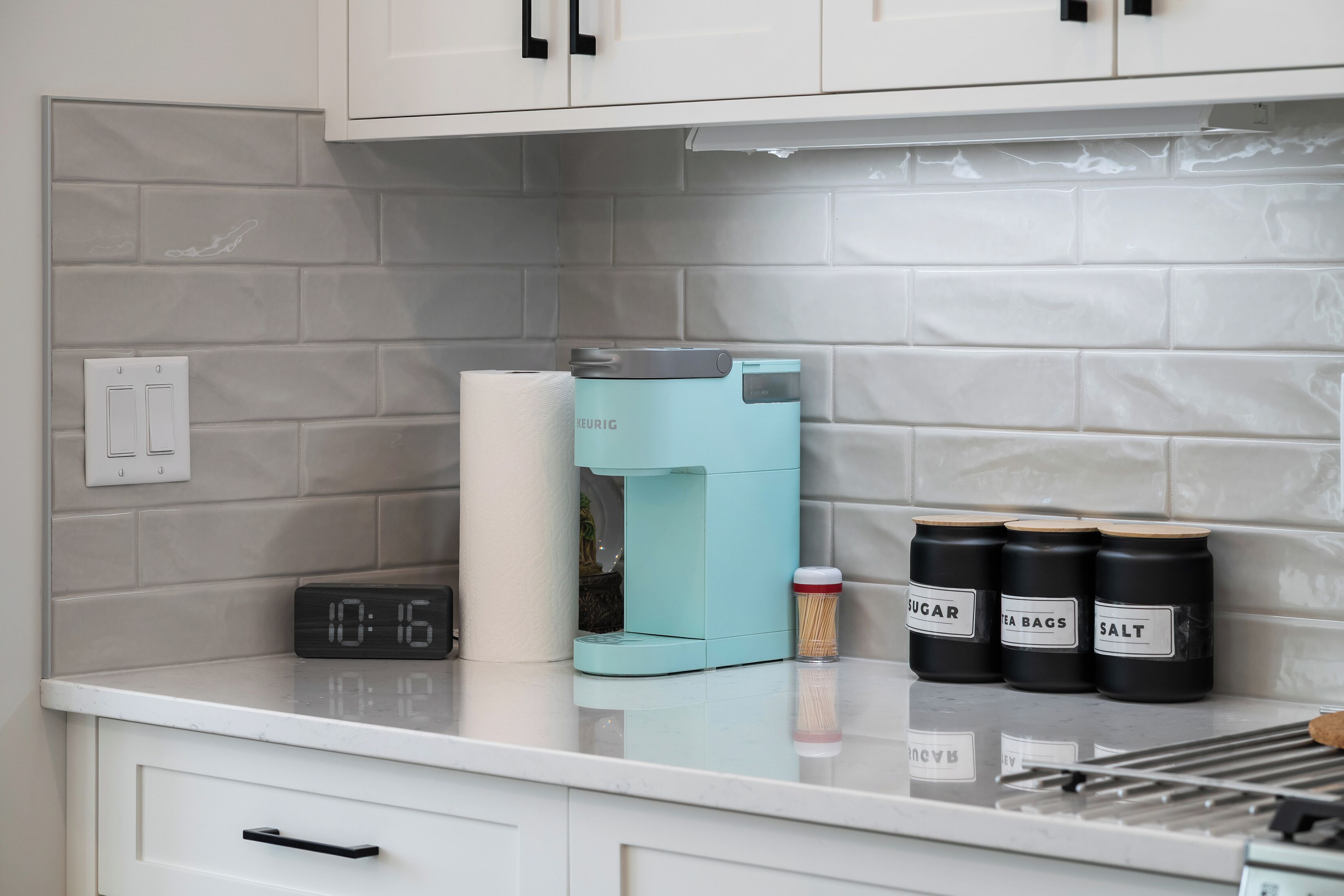 Une cuisine équipée d’une machine à café, d’une horloge et de bocaux étiquetés « sucre », « sachets de thé » et « sel ».