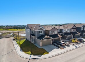A residential area with multiple houses, a paved driveway, and a grassy area. - Creekstone Retreat - South West Calgary - A Cozy Home for a Peaceful stay (Calgary)