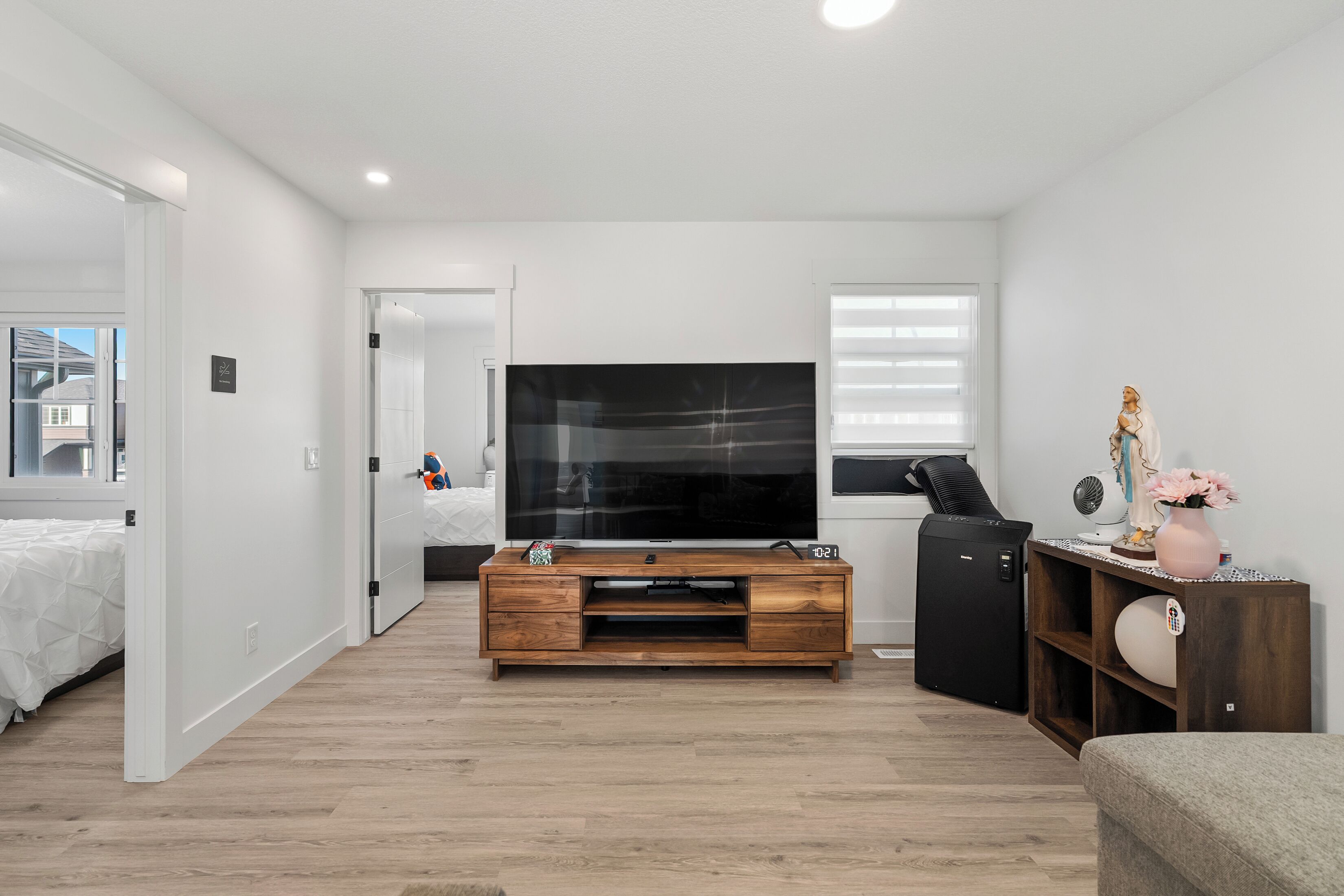 A modern living room with a flat-screen TV, wooden entertainment unit, and a small refrigerator.