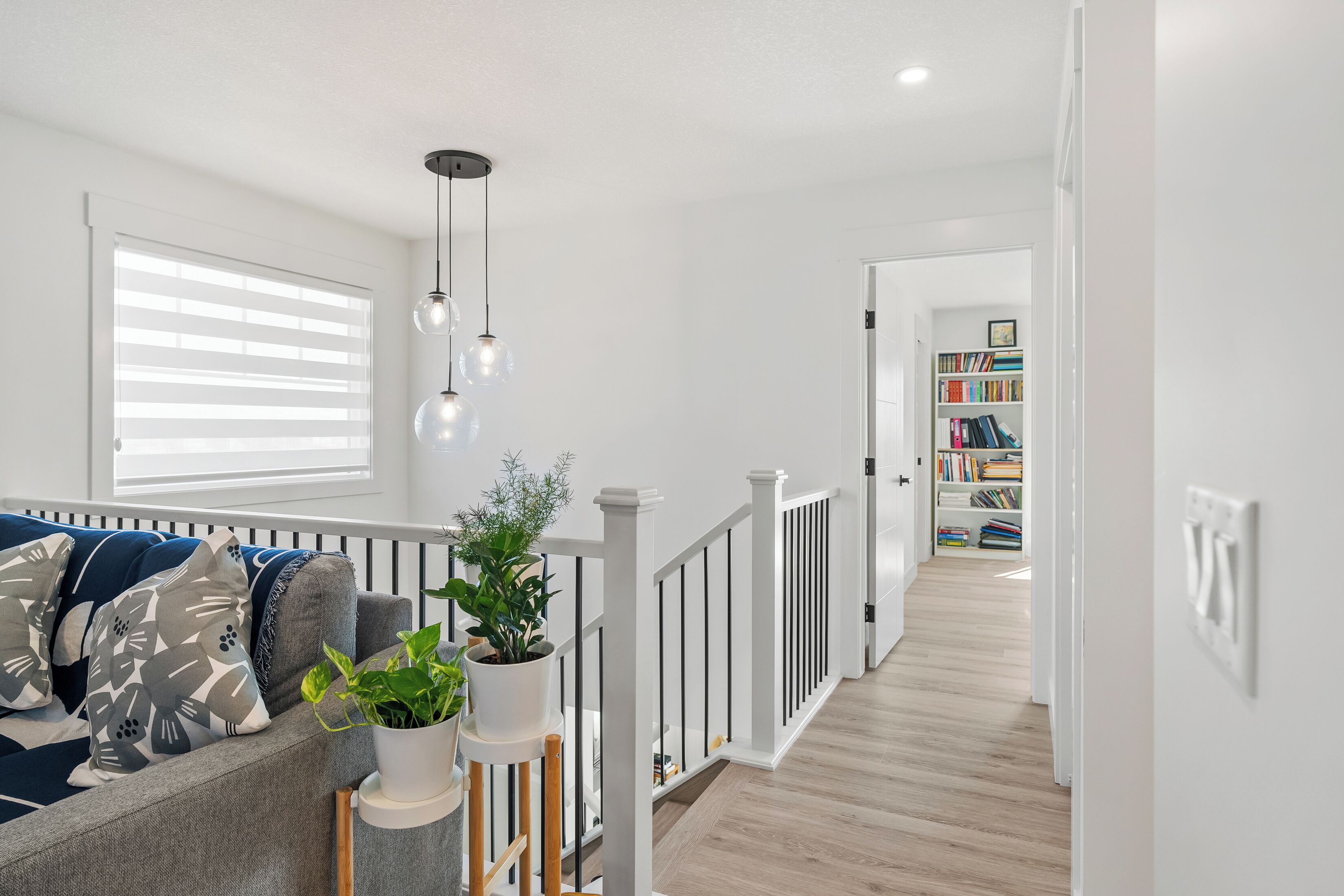 A modern living room with a sofa, a potted plant, and a staircase leading to a bookshelf.